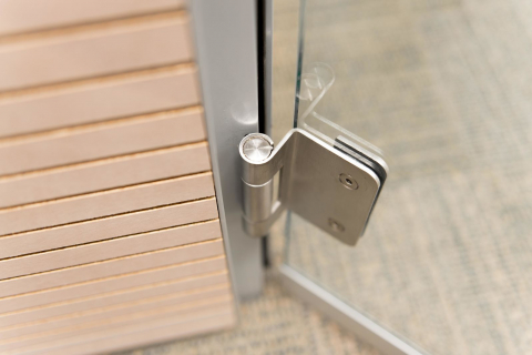 Detail of a stainless steel hinge of a DK42 door frame and a tampered glass door